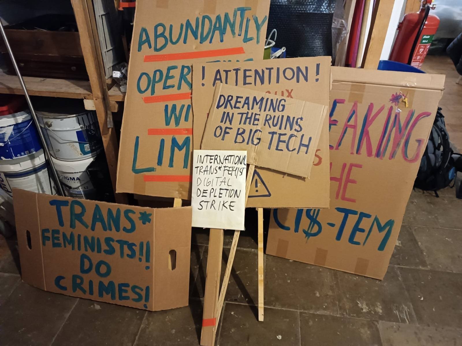 Stack of picket-signs: "Dreaming in the ruins of Big Tech", "Abundantly Operating with Limits", "Trans*Feminists Doing Crime"