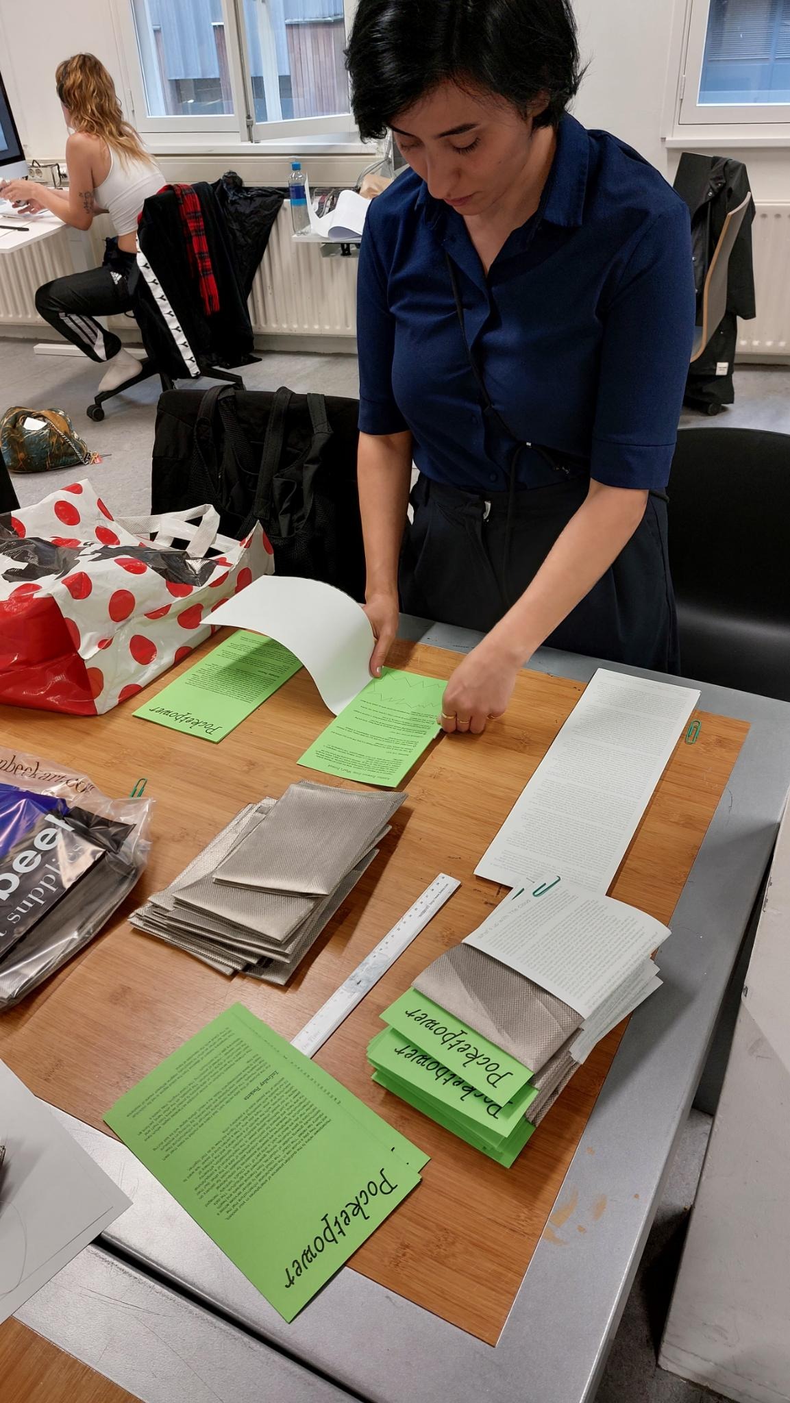 "A person folding papers and silver fabric into a package, reading "Pocket Power"