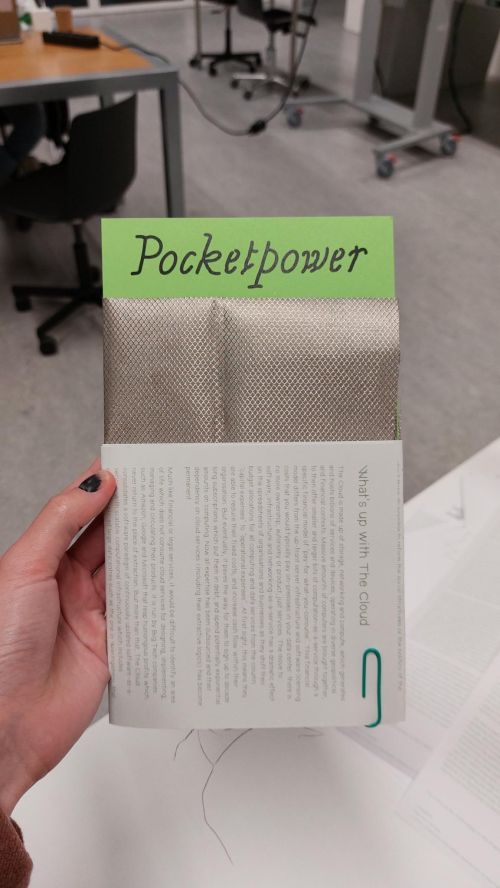 A person holding a package containing silver fabric, folded into a green paper, reading "Pocketpower