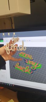 A picture of a hand holding two 3d printed words in front of a screen of two new words being prepared to print.