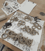 Various coiled letters, per, per, p, e, go, go, slow, go slow, goslow. Laying on a painted paper, ready to dry.
