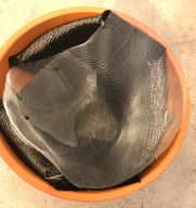 metallic Mesh and carbon cloth wrapped inside a orangey-brown ceramic pot. The carbon cloth is on the inside, touching the pot, and the mesh is wrapped on the inside of the cloth.